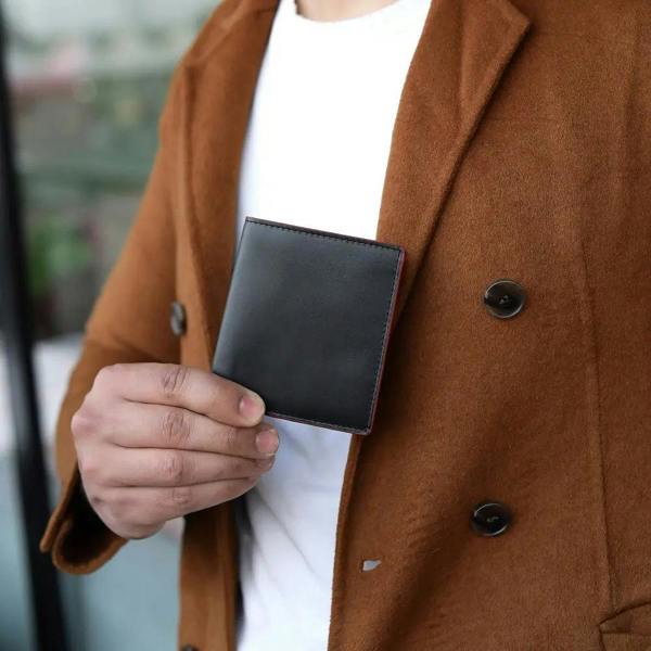 Person wearing a brown coat holding a black wallet.