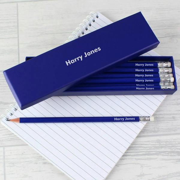 A dark blue personalised gift box and matching pencils printed with the name Harry Jones resting on a spiral notepad.