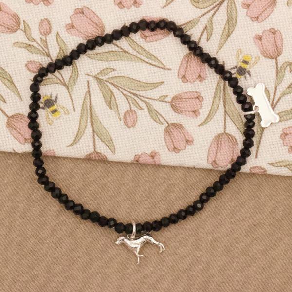 Black beaded necklace with a silver pointer dog charm on a floral-patterned fabric background
