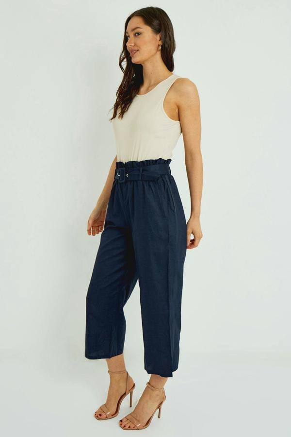 Woman wearing a white sleeveless top and navy blue high-waisted pants on a white background