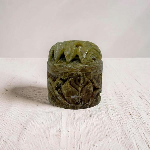 Carved stone container with floral patterns on a white surface