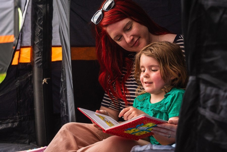 a mother & daughter read inside the Discovery Inflatable Tents darkened sleeping pod