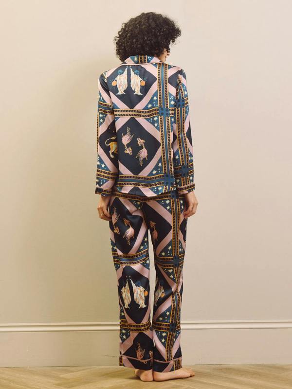 Woman wearing a celestial patterned satin pyjamas standing against a plain wall.