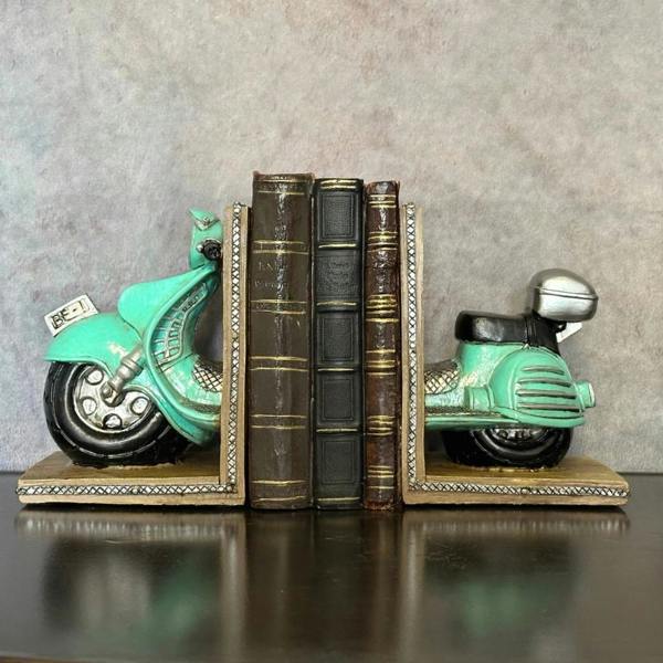 A pair of vintage mint green polyresin scooter bookends holding three antique books together on a rustic wooden sideboard cabinet under retro scooter tin signs.