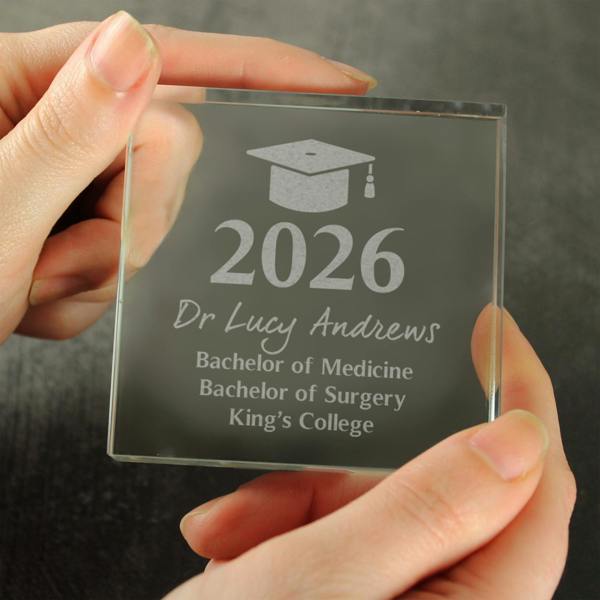 A close-up of a person holding a personalised graduation crystal token engraved with the year 2026, a name, and degree details.
