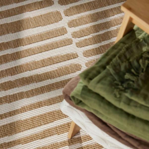 Close-up of a striped rug with a wooden stool and green fabric.