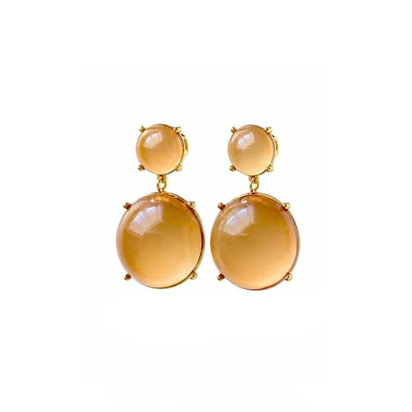 A pair of gold drop earrings featuring large, smooth oval amber-colored gemstones and smaller round studs above them, set against a plain white background.
