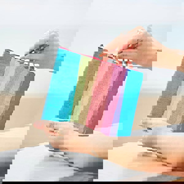 A woman holding a Recycled Plastic Rainbow Pouch on the beach.