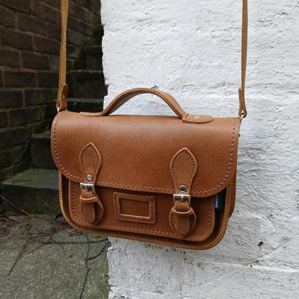 Brown leather satchel bag with a strap against a white wall.