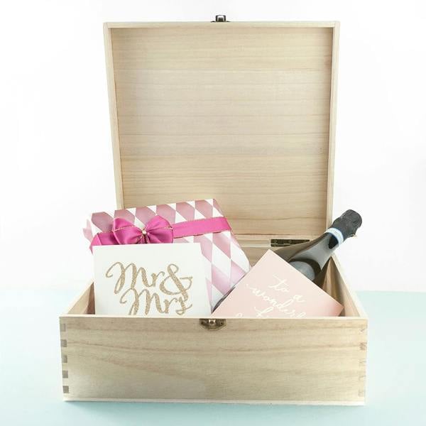 An open natural pine wooden memory box filled with a bottle of champagne, a pink-ribboned gift, and a gold glitter 'Mr & Mrs' card.