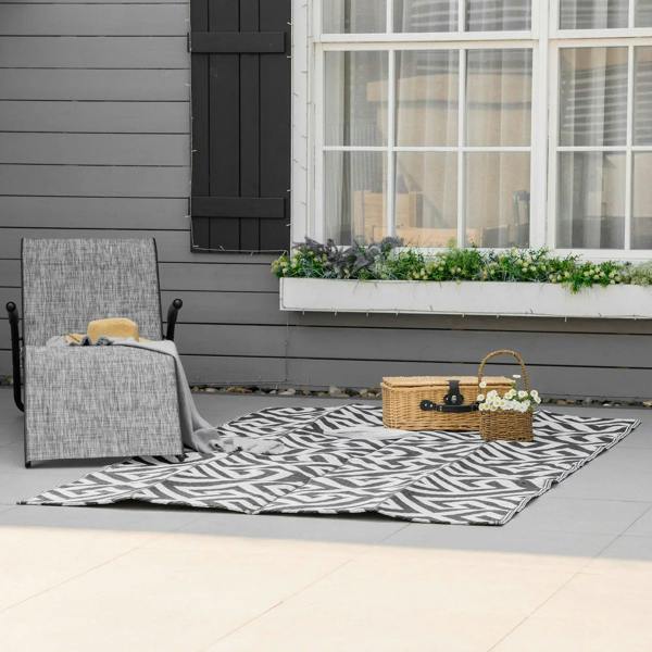 Black-and-white reversible outdoor rug laid flat on patio tiles with Greek key pattern.