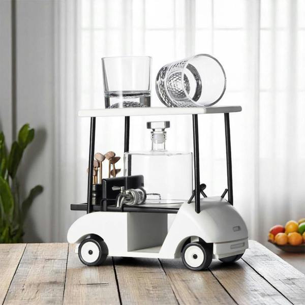 A white and black miniature golf cart decanter stand with a spigot dispenser and two whiskey glasses on top.