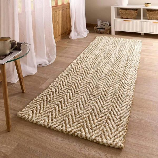 Beige woven runner rug on a wooden floor with a side table and curtains in the background.