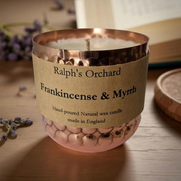 Candle with a label reading 'Ralph's Orchard Frankincense & Myrrh' on a wooden surface.
