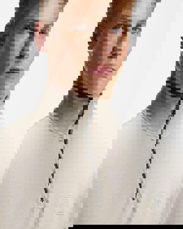 Man wearing a beige high-neck sweater with a zipper on a light gray background