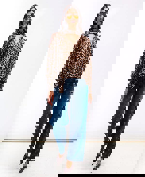 Woman wearing a leopard print top and blue jeans on a white background