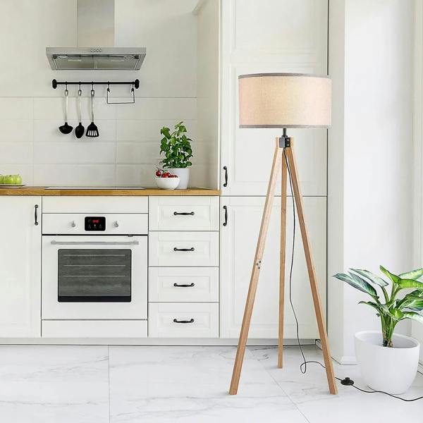 Beige fabric floor lamp shade on light wood tripod legs with black cable and plug