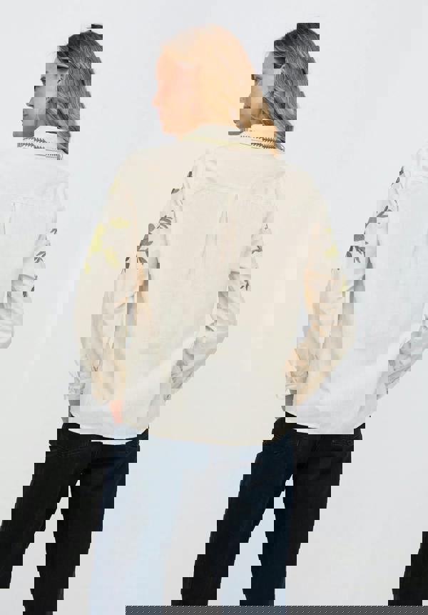 Woman wearing a beige blouse with green floral embroidery on a white background