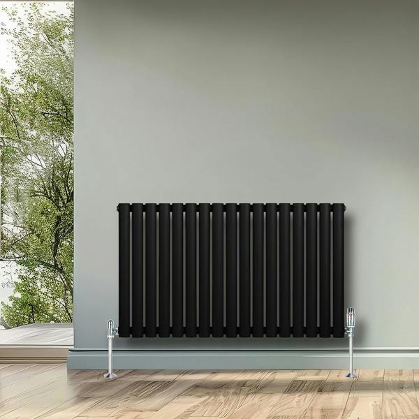 Sleek black oval single column radiator with chrome valves, mounted on a light gray wall, enhancing a modern interior space