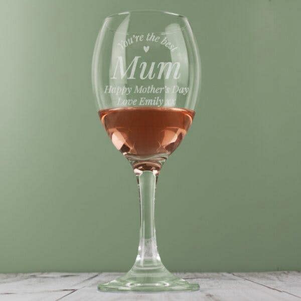 A personalised wine glass from Abode Home & Gifts filled with rosé wine against a sage green background.