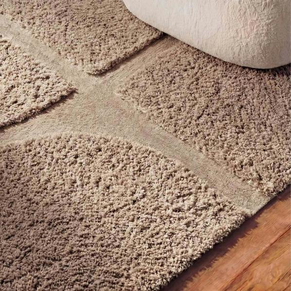 Close-up of a beige carpet being rolled out on a wooden floor.