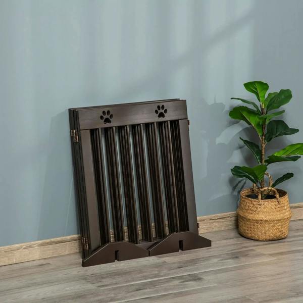 Brown wooden pet gate standing with support feet and paw print cutouts on top bar