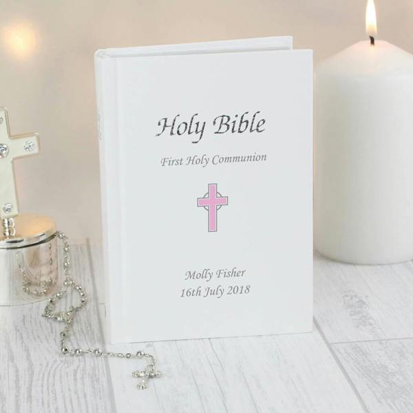 A white leatherette Holy Bible personalised for Molly Fisher with a pink cross, next to a silver rosary and a burning candle.