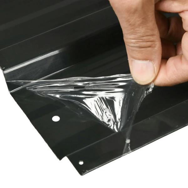 Dark grey corrugated steel roof panel corner with protective plastic wrap and hole
