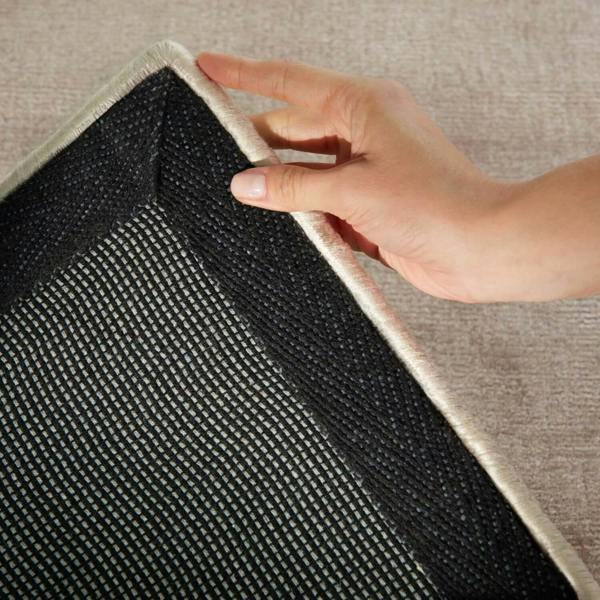 Hand pulling a rug off the floor with a textured surface.