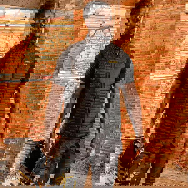 Stanley Banff Mens Ripstop Water Resistant Work Gilet Body Warmer, black sleeveless padded vest worn by a man in a construction site with brick walls.