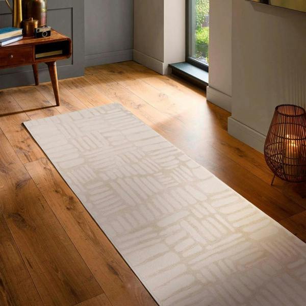 White geometric patterned rug on a wooden floor with a lamp and small table in the background.