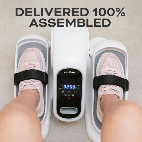 Someone in pink sneakers uses the Reviber Motorised Mini Elliptical Bike with foot straps, set on light carpet. The display shows “0259.” Above, the text reads: “DELIVERED 100% ASSEMBLED.”.
