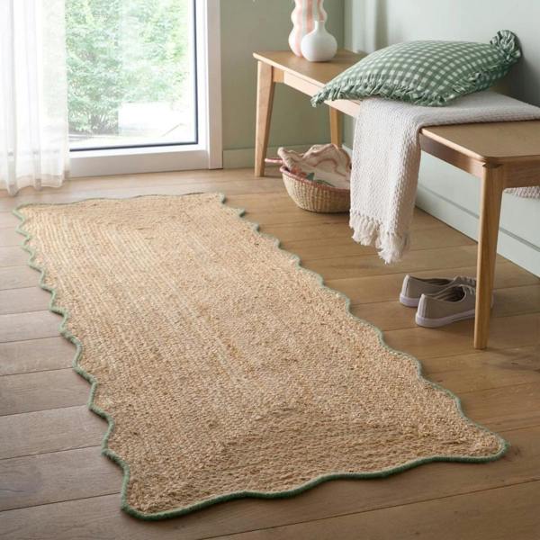 Beige woven rug on a wooden floor with a bench and window in the background