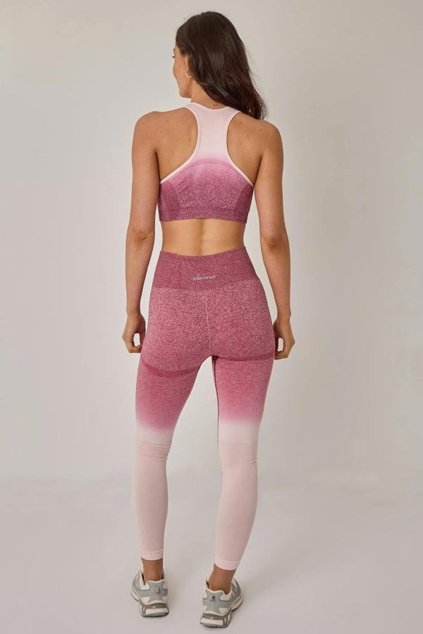 Woman wearing a pink and white gradient sports bra and leggings set on a plain background