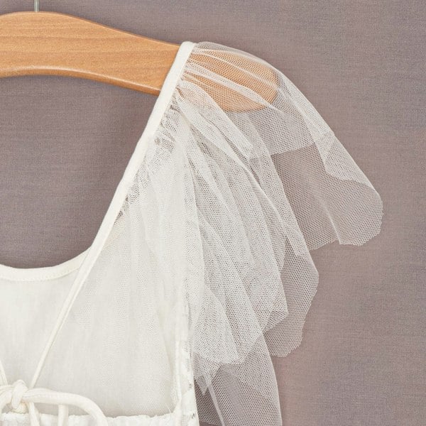 White shoulder of flower girl dress on a hanger against a gray background