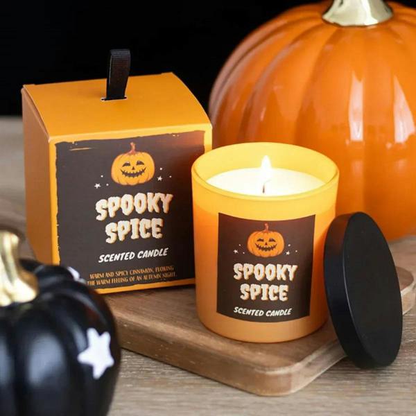 Spooky scented candle in orange jar with black lid, lit flame, gift box nearby