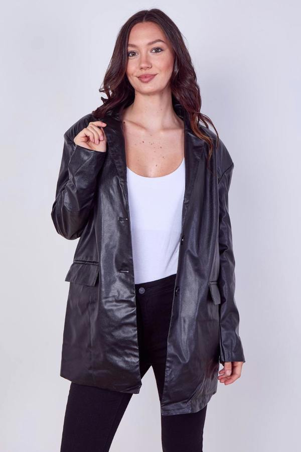 A woman modeling a black faux-leather jacket over a white tank top and black pants, standing against a light gray studio background.
