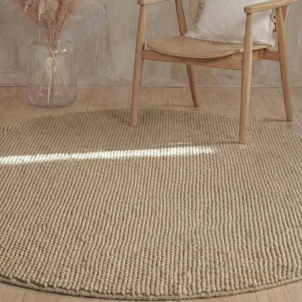 Beige textured rug with a wooden chair and vase in the background