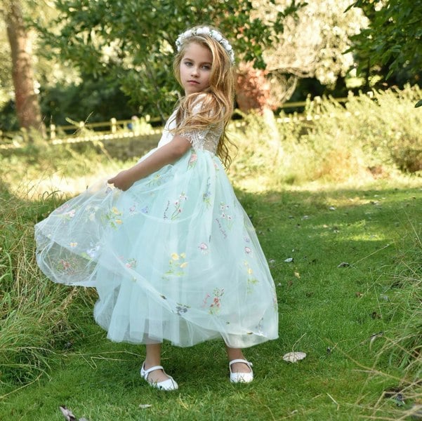 Young girl in a light blue floral dress standing in a grassy outdoor setting.