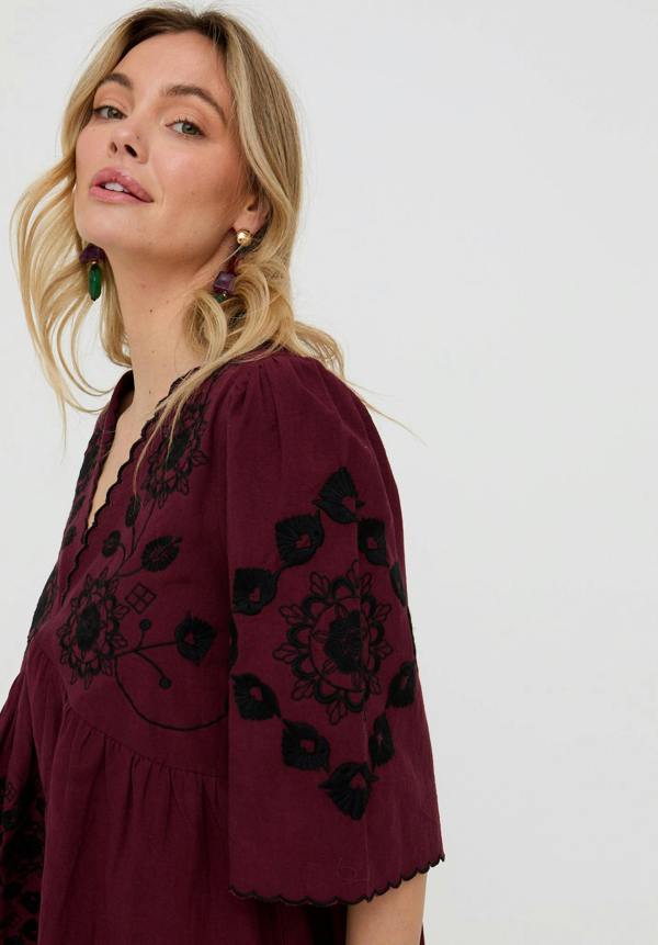 Woman wearing a burgundy dress with black floral embroidery on a white background