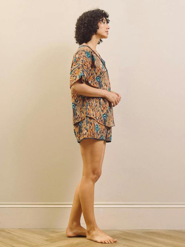 Woman wearing a feather patterned short pyjama set standing against a plain wall.