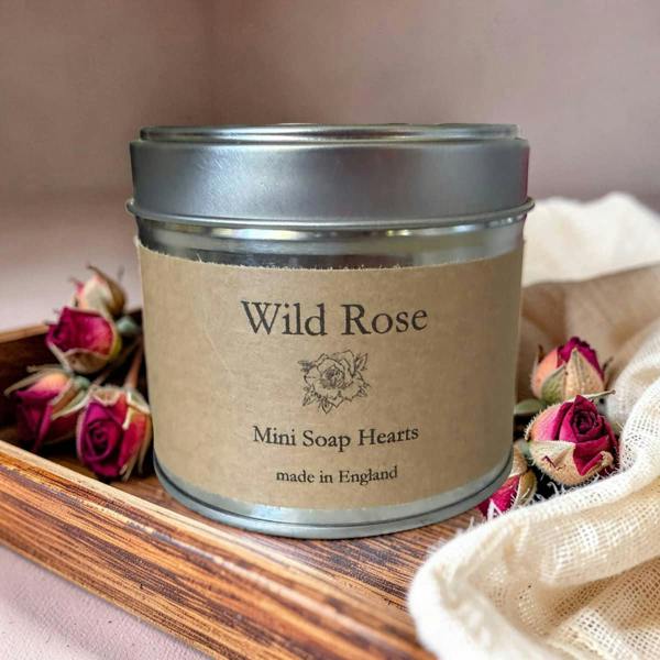 Tin labeled 'Wild Rose Mini Soap Hearts' on a wooden tray with dried roses.