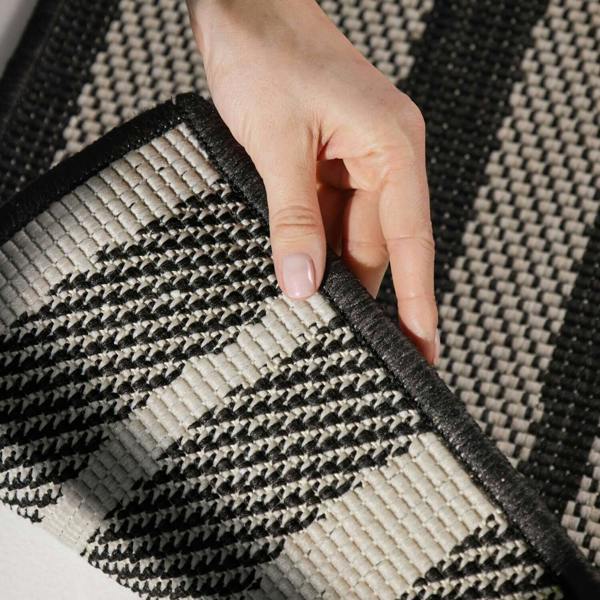 Hand holding a corner of a black and beige patterned rug
