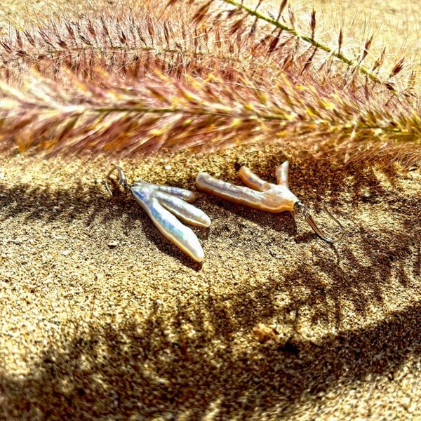 Irregular baroque pearl earrings photographed on a sandy beach.