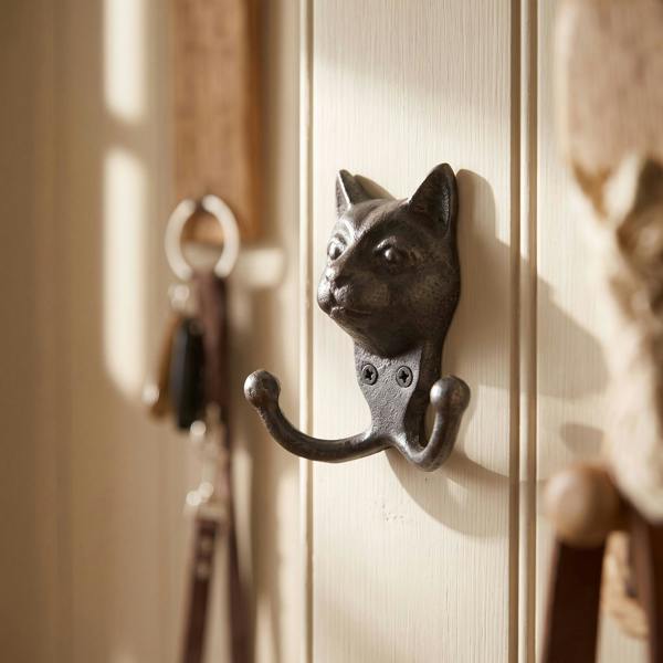 Close-up of a cast iron novelty cat coat hook on a painted wall, showcasing its textured surface and whimsical design in a cozy home entryway.