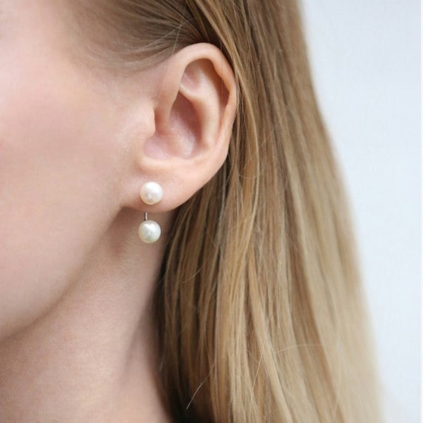 A close up of an ear with double pearl ear jacket earrings.