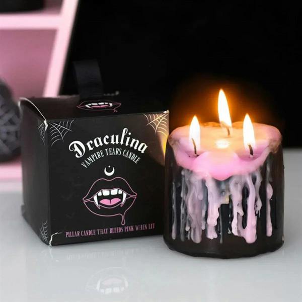 Small black pillar candle with pink wax top and pink drips, three lit wicks