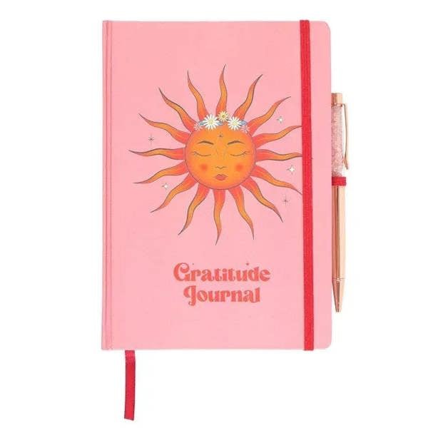 Pink gratitude journal with sun illustration cover and red ribbon spine; rose quartz pen
