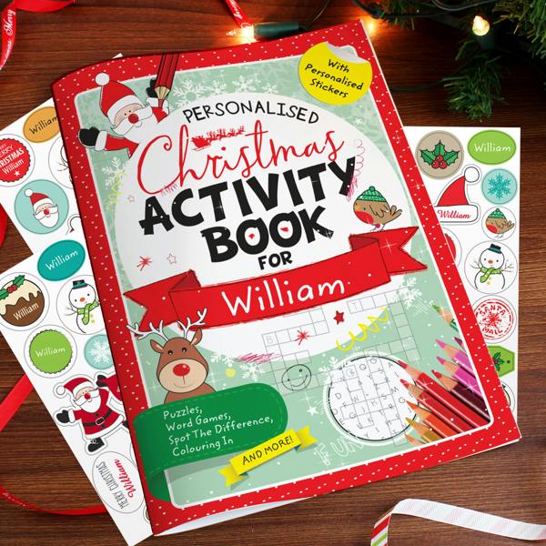 Personalised Christmas Activity Book for William displayed on a wooden surface surrounded by personalised sticker sheets, pencils, and festive ribbon