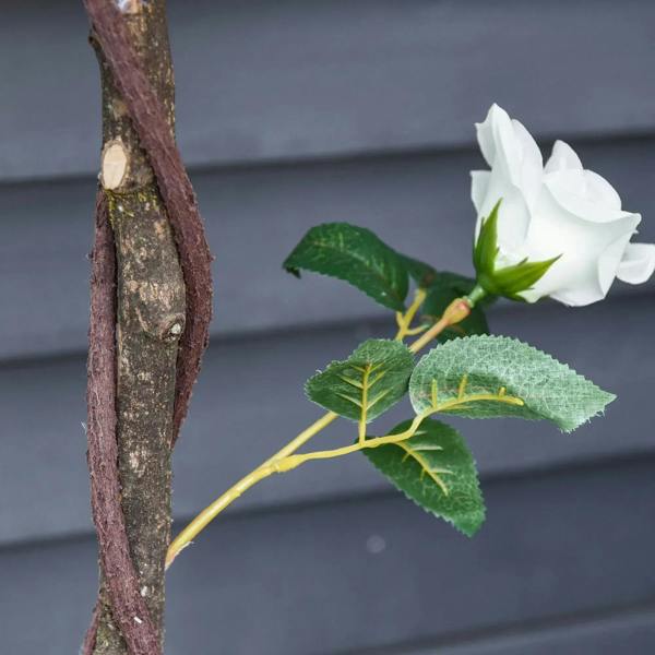 Artificial white rose bloom with green leaves on brown tree trunk